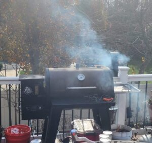 Pellet smoker with smoke rising while a Thanksgiving turkey cooks on a backyard deck