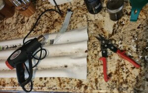 Plastic roofing panel being cut with tin snips and flattened using a heat gun